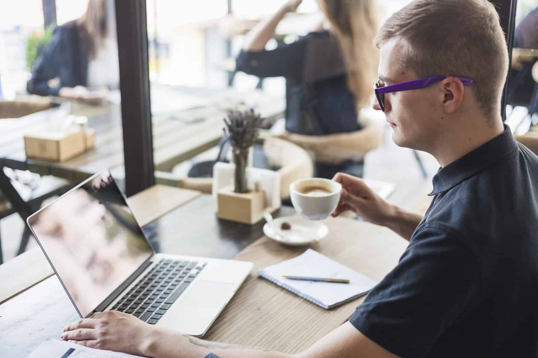 Man drinks coffee at café while doing e-learning.