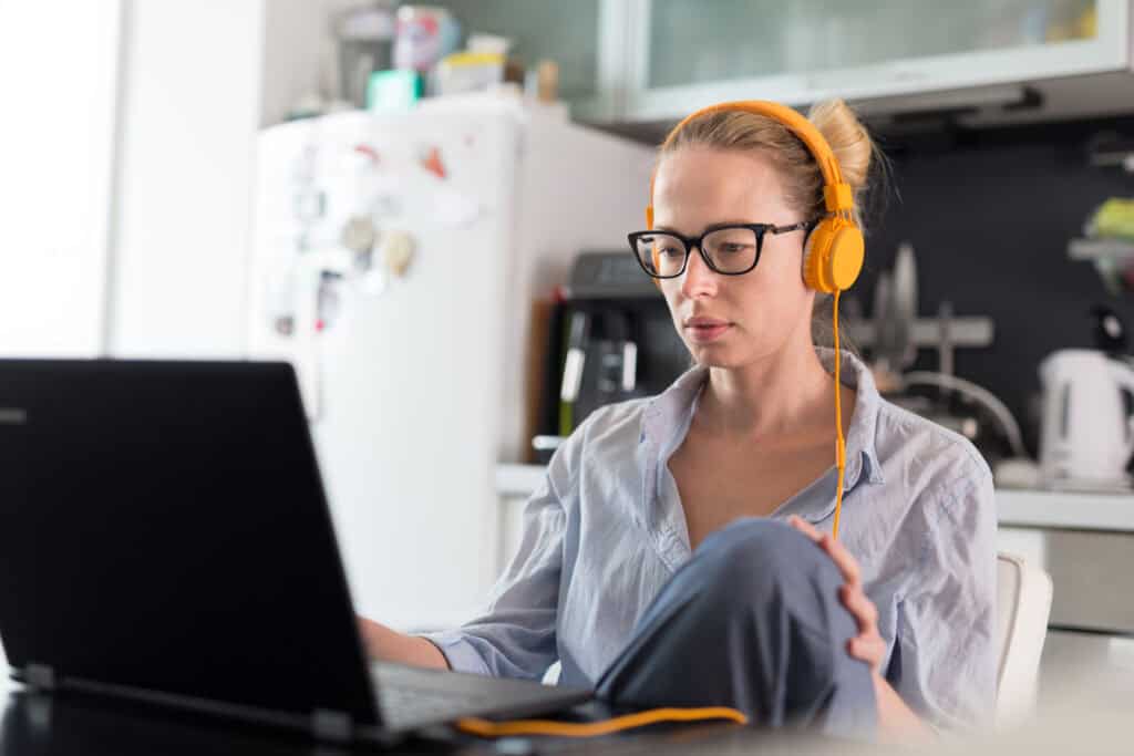 Woman sits in kitchen while doing e-learning.