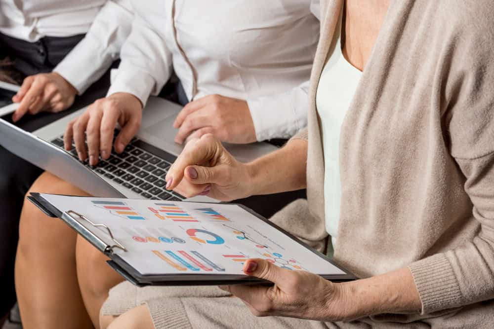 One women with a computer and another with a clipboard discuss.