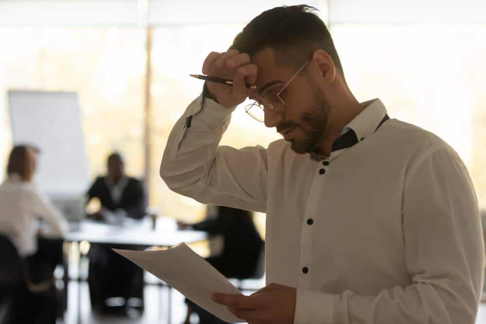 Stressed man wipes sweat while looking at a document.