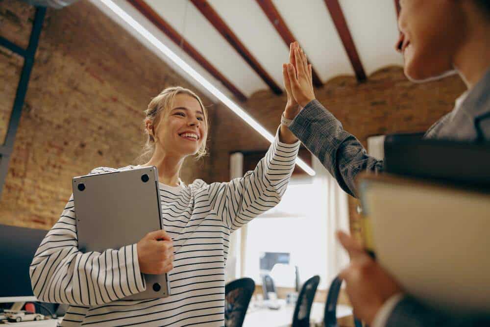 Two female colleagues giving each other high five while smiling.