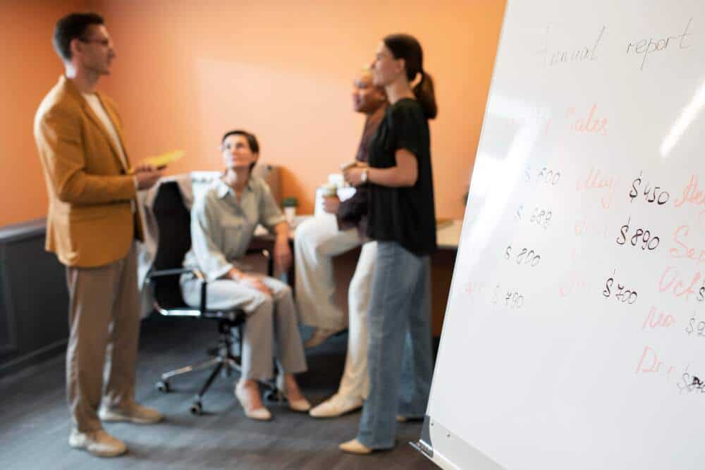 A whiteboard with colleagues discussing in the background.