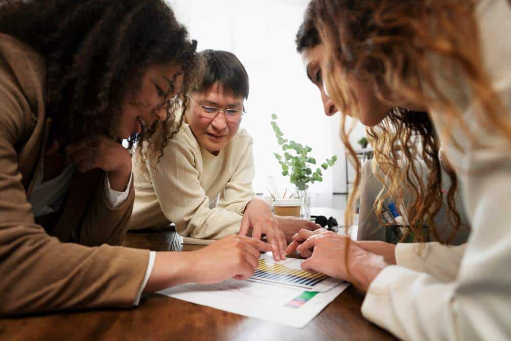 Three people leaning over a table and discussing a sheet of statistics
