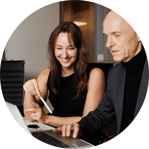 Two people collaborating at a laptop, smiling and engaged in discussion in an office setting.