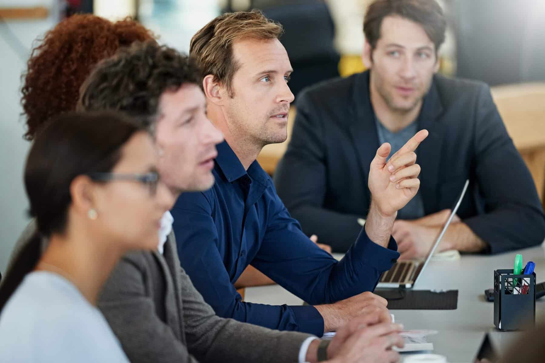 Colleagues sitting around a table while one man raises his hand to say something