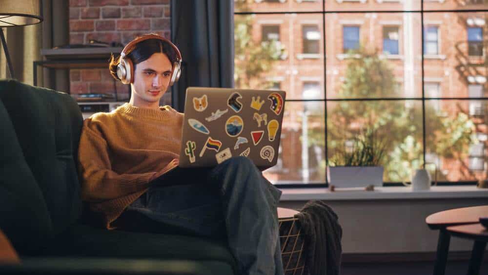 Male learner sitting on a couch with headphones on and a laptop on his lap