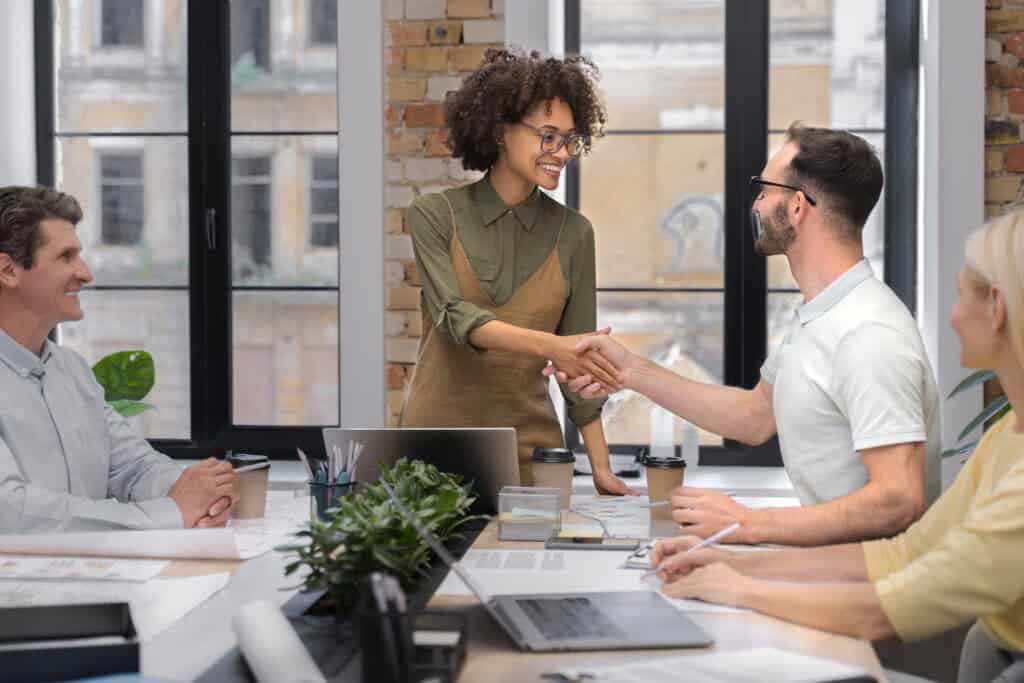 Smiling professionals shaking hands across a meeting table, symbolizing lead conversion or client onboarding
