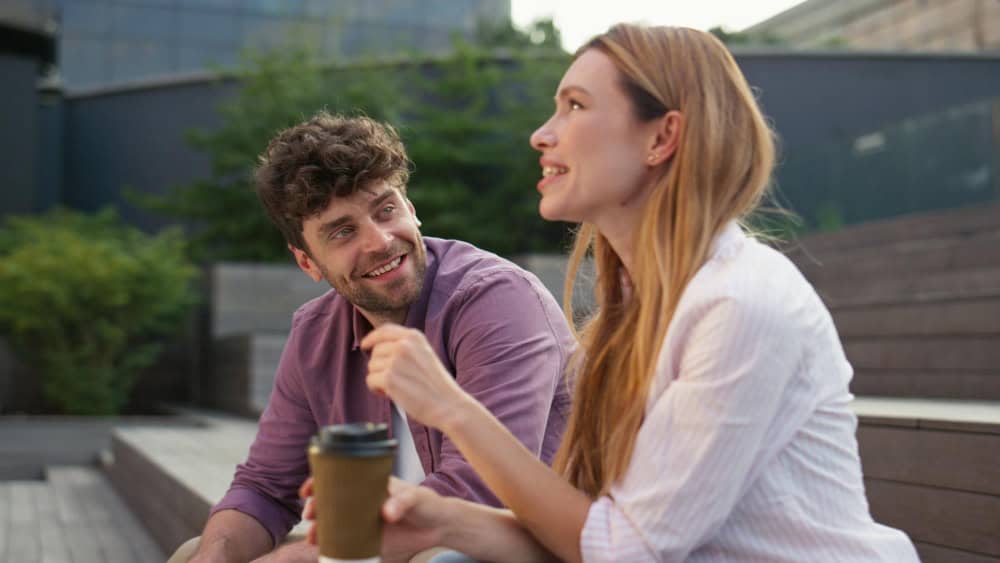 Two new colleagues trying to loosen up the mood by playing an icebreaker game while sitting outside with a coffee in hand