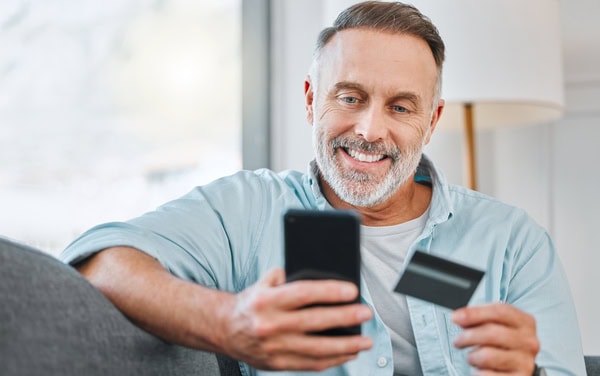 Man paying for a training course on his phone Smiling adult man completes online payment for a maritime training course on his smartphone while holding a credit card.